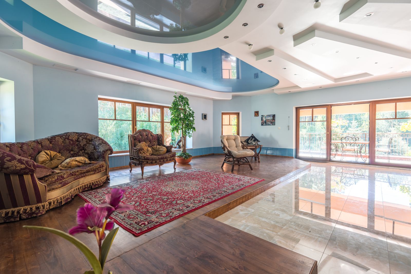 Spacious living room with a glossy blue multi-level stretch ceiling, light blue walls, and tall windows