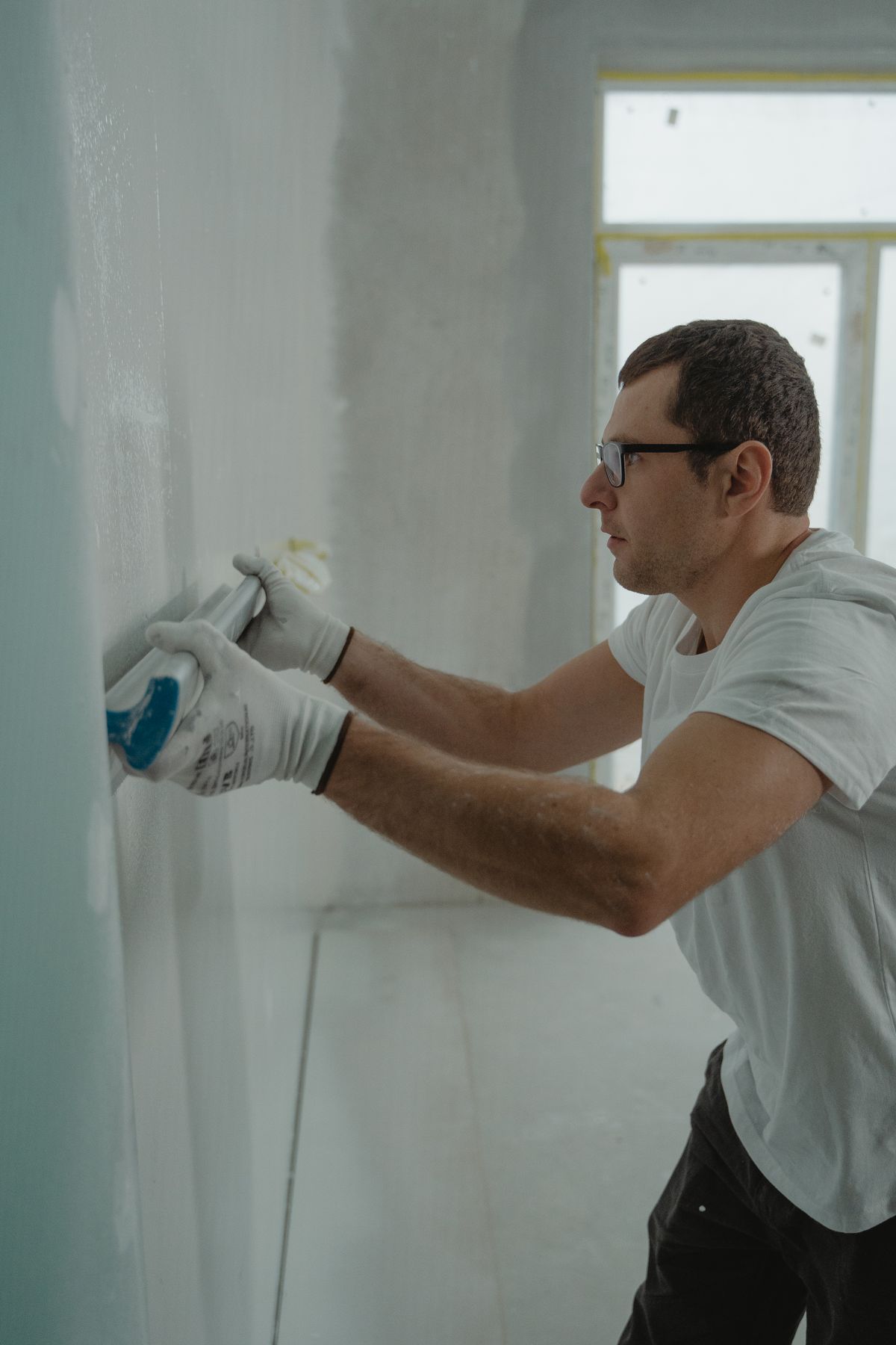 Tradesman in work gloves pressing a strip of compound smooth on a patched wall surface