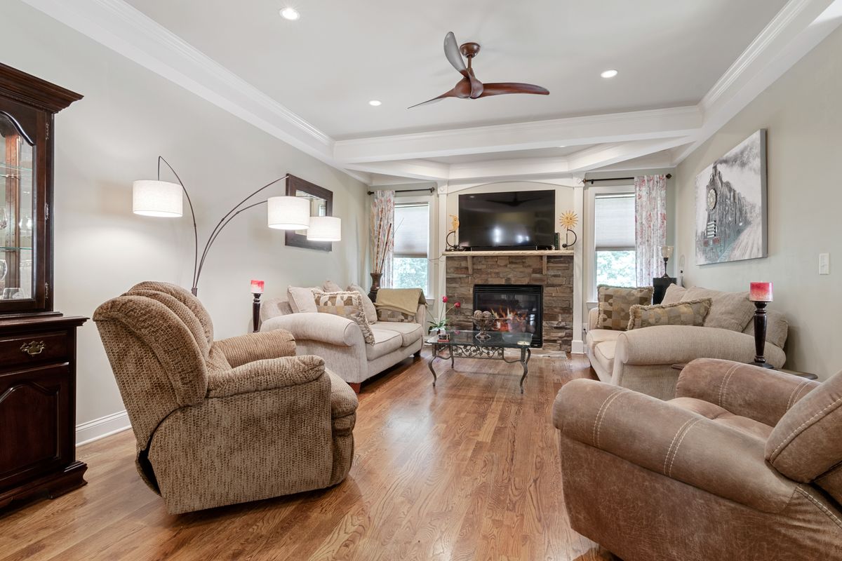 Living room with a smooth tray ceiling, crown molding, ceiling fan, and stone fireplace